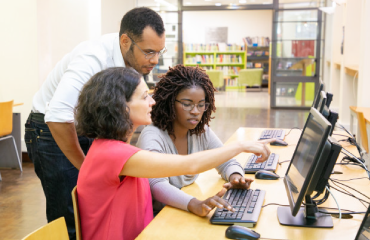 Two Women And a Man In Library Looking At Computer
