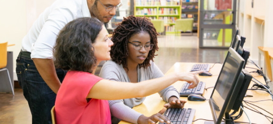 Two Women And A Man In Library Looking At Computer